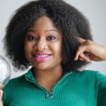 Idea Opportunity - Positive young African American lady holding light bulb in hand on gray background