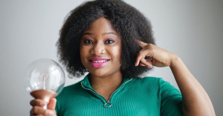 Idea Opportunity - Positive young African American lady holding light bulb in hand on gray background