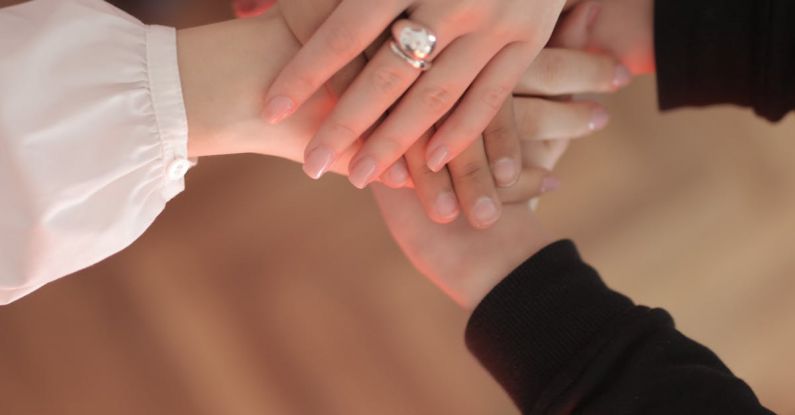 Trust Handshake - Top view of faceless friends in different clothes stacking hands together while standing on wooden floor indoor on sunny day