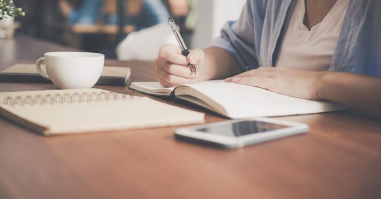 Technology Learning - Woman Writing on a Notebook Beside Teacup and Tablet Computer