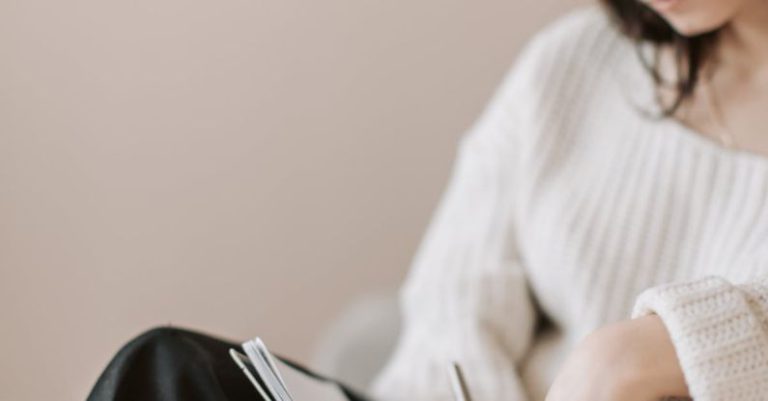 Delegation Task - Attentive female wearing eyeglasses and casual outfit sitting barefoot with crossed legs on comfortable couch in modern flat and taking notes in notebook with pen