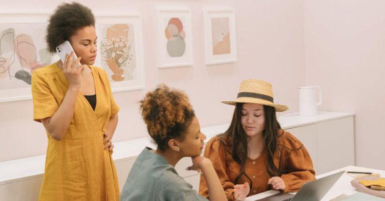 Leader Branding - A Woman in Yellow Dress Talking on the Phone while Looking at Her Colleagues Sitting Near the Laptop