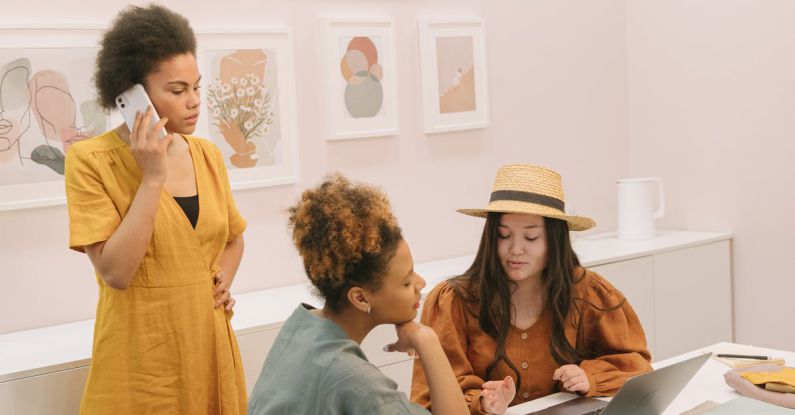Leader Branding - A Woman in Yellow Dress Talking on the Phone while Looking at Her Colleagues Sitting Near the Laptop