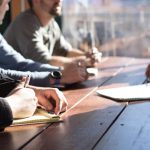 Career - people sitting on chair in front of table while holding pens during daytime