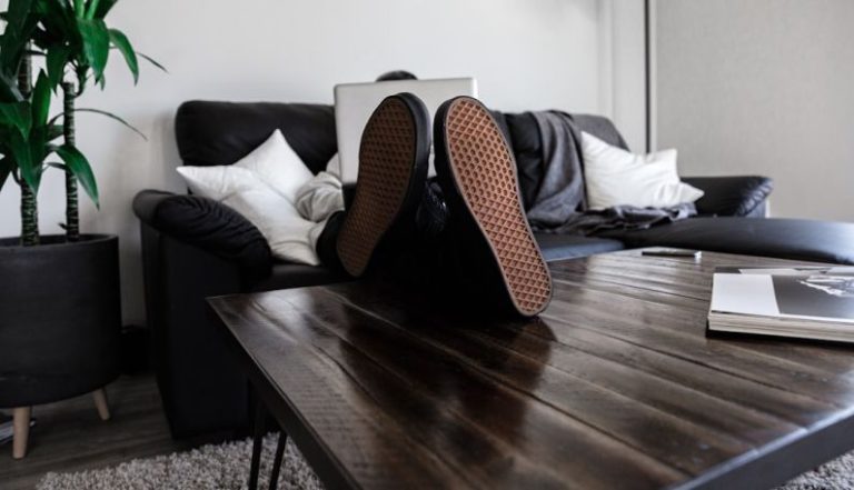 Relax Work - person sitting on sofa resting its feet on top of coffee table while using laptop
