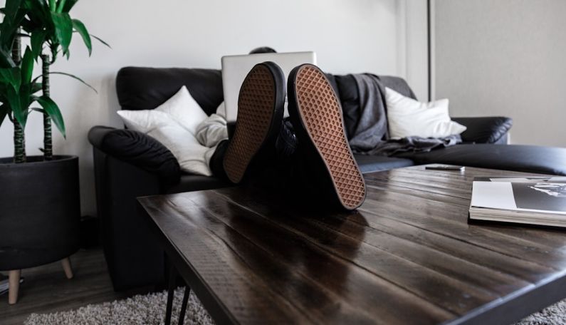 Relax Work - person sitting on sofa resting its feet on top of coffee table while using laptop
