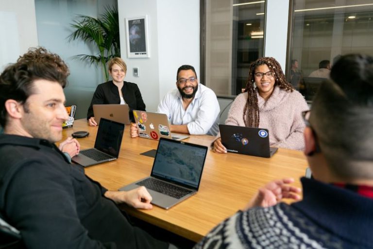 Leadership - four people all on laptops, two men and two women, listen to person talking in a board meeting