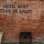 Financial Stability - Until debt tear us apart printed red brick wall at daytime