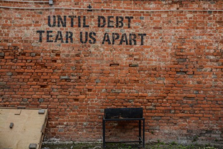 Financial Stability - Until debt tear us apart printed red brick wall at daytime
