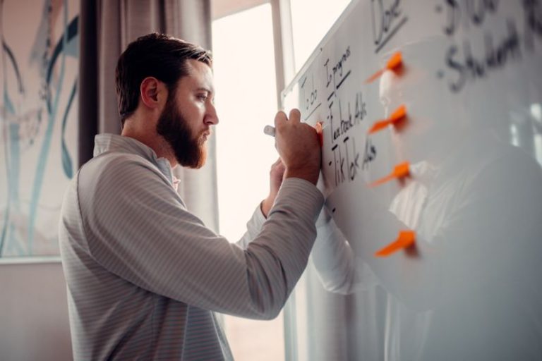 Entrepreneurship - a man writing on a white board with orange markers