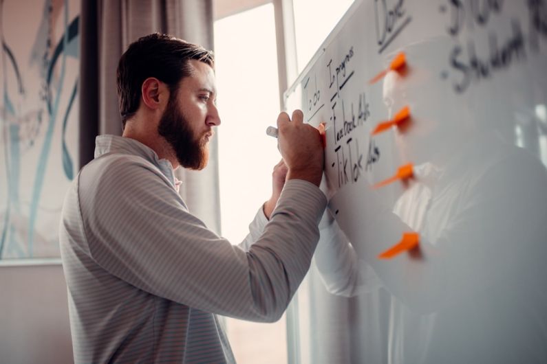 Entrepreneurship - a man writing on a white board with orange markers