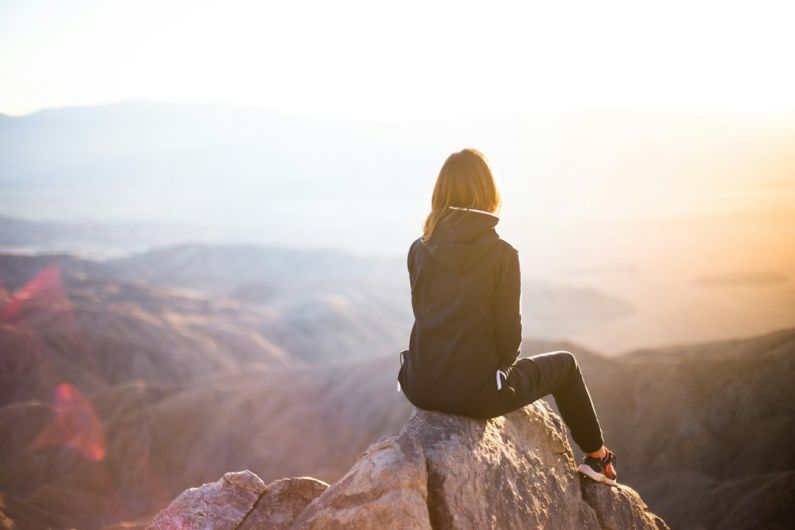 Lifestyle - person sitting on top of gray rock overlooking mountain during daytime