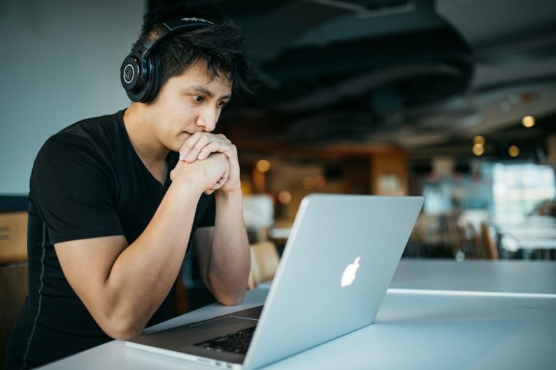 Learning - man wearing headphones while sitting on chair in front of MacBook