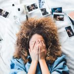 Memory - woman lying on bed covering her face surrounded by photos and white camera