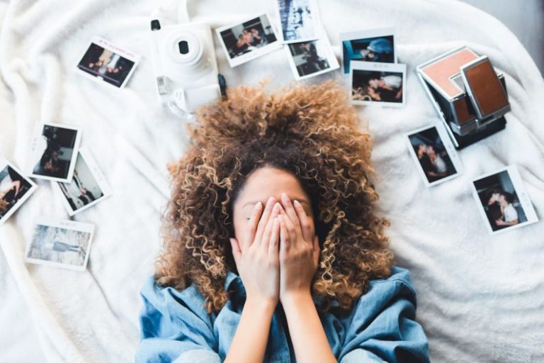 Memory - woman lying on bed covering her face surrounded by photos and white camera